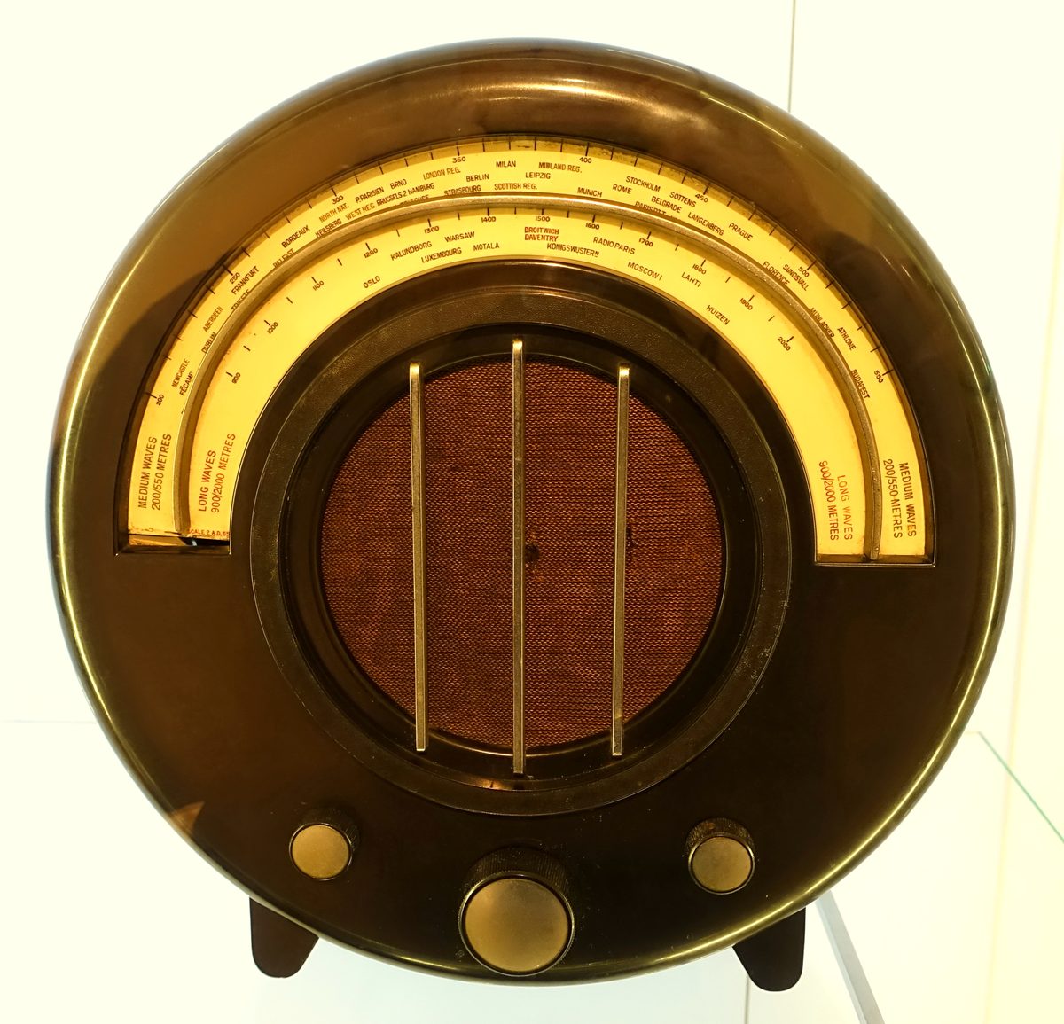 A round brown Bakelite radio with a curved station dial, a cloth speaker grille and three knobs