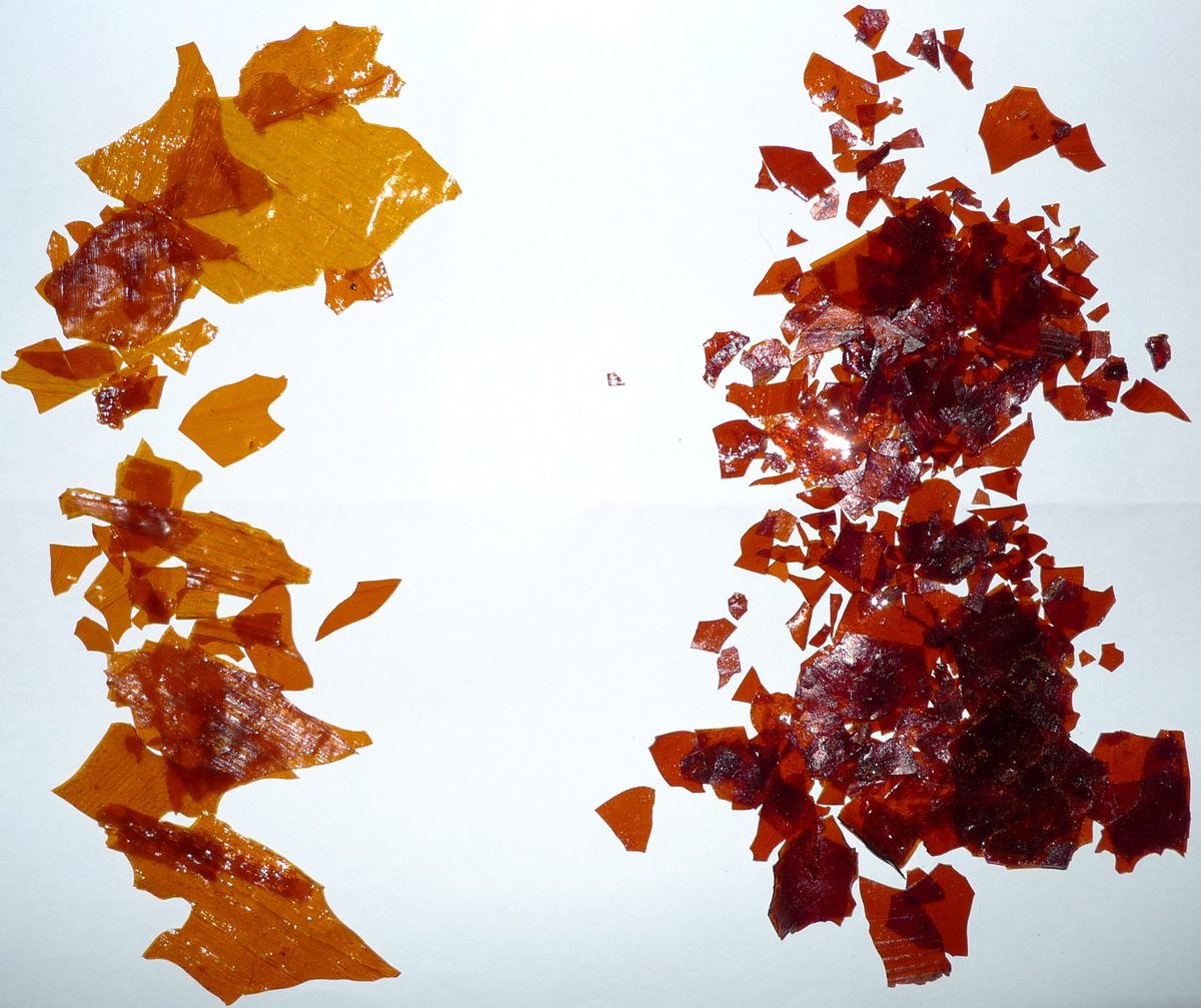 Two piles of amber and dark red shellac flakes on white paper