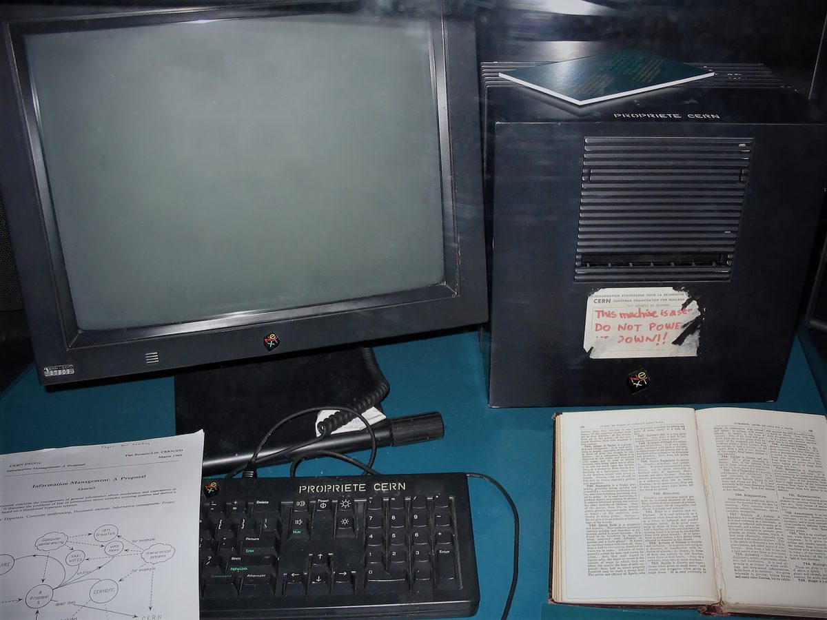 A black NeXT computer and monitor in a museum case, with a handwritten label on the computer reading "This machine is a server. DO NOT POWER IT DOWN!!"
