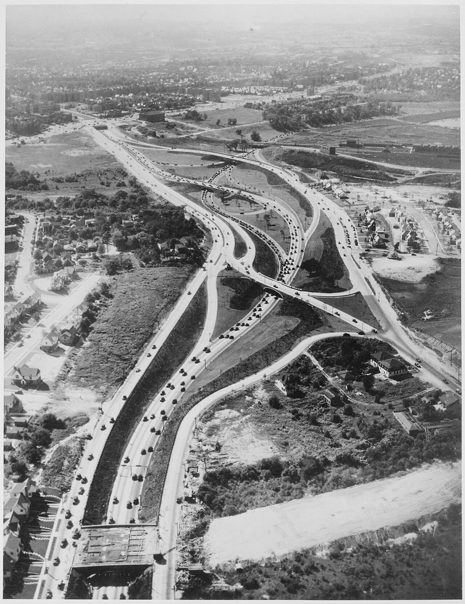Aerial view of cars streaming along the Grand Central Parkway through a looping interchange among houses and fields
