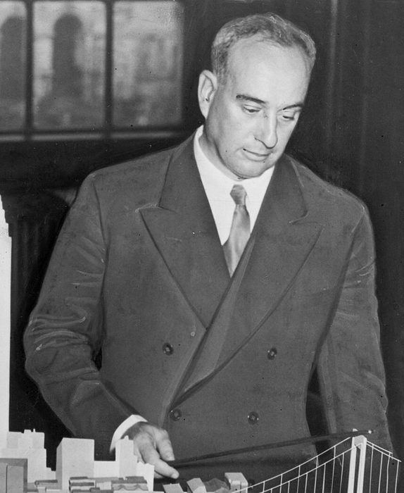 Robert Moses in a double-breasted suit, pointing at a model of a proposed bridge