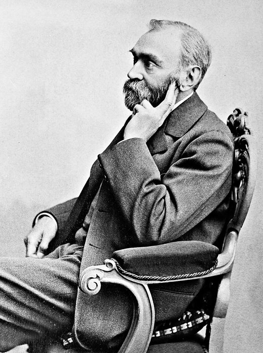 Photograph of Alfred Nobel seated sideways in a chair, bearded, his chin resting on his hand