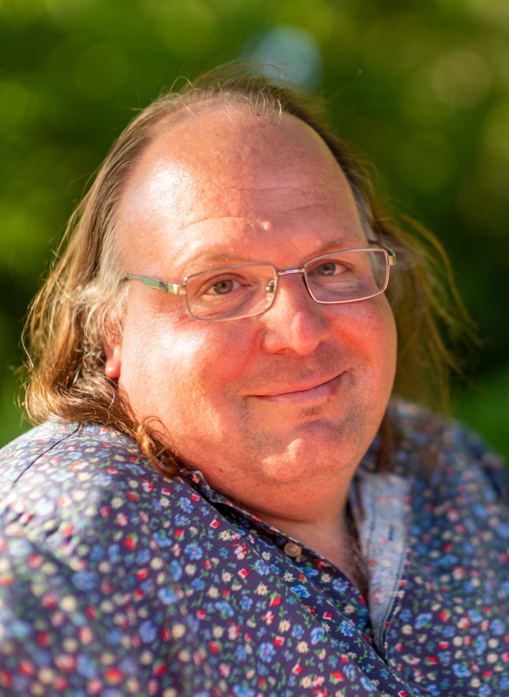 Ethan Zuckerman smiling outdoors, with long hair, glasses and a blue floral shirt